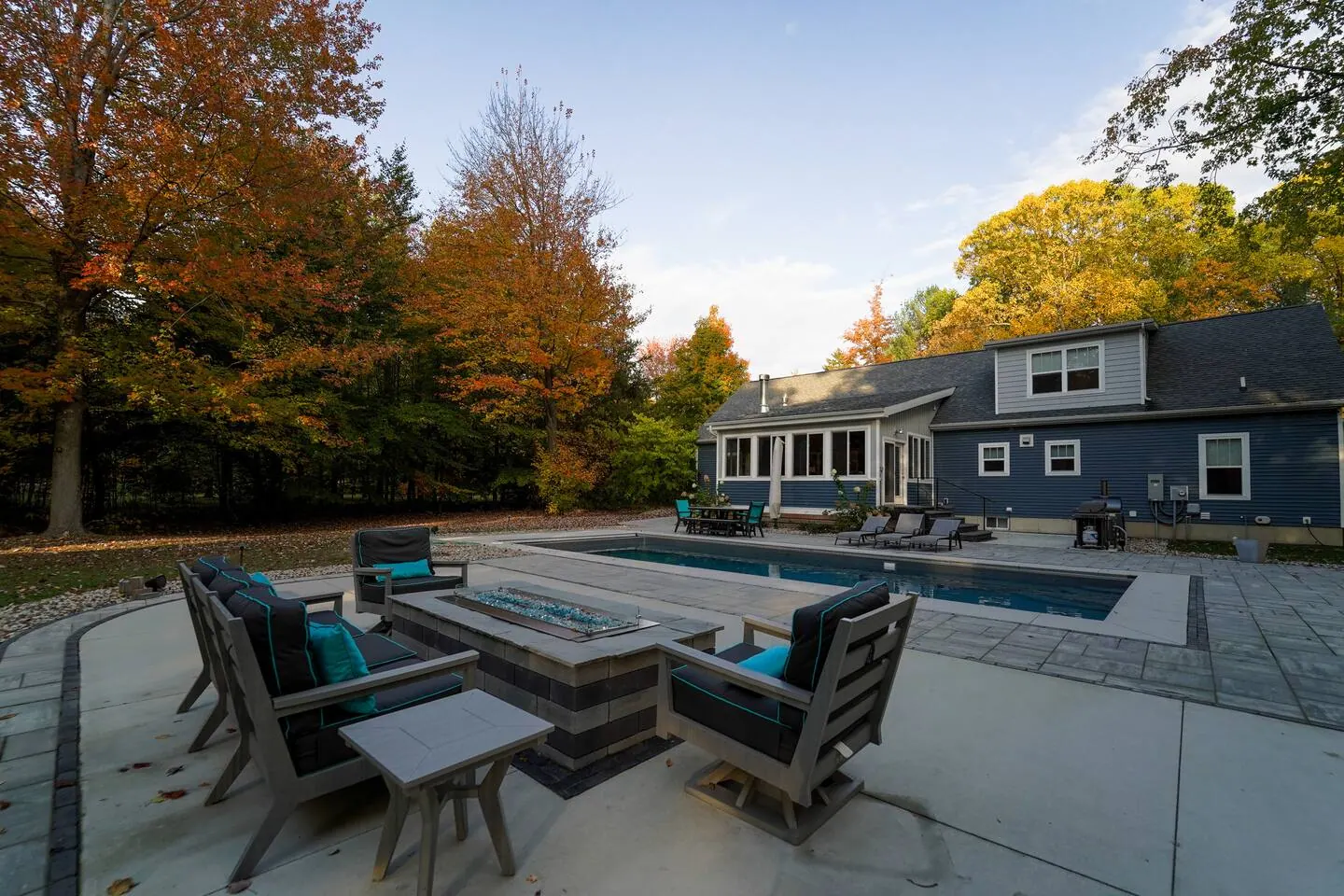 Autumn patio with lounge chairs, fire table, pool, and the house beyond